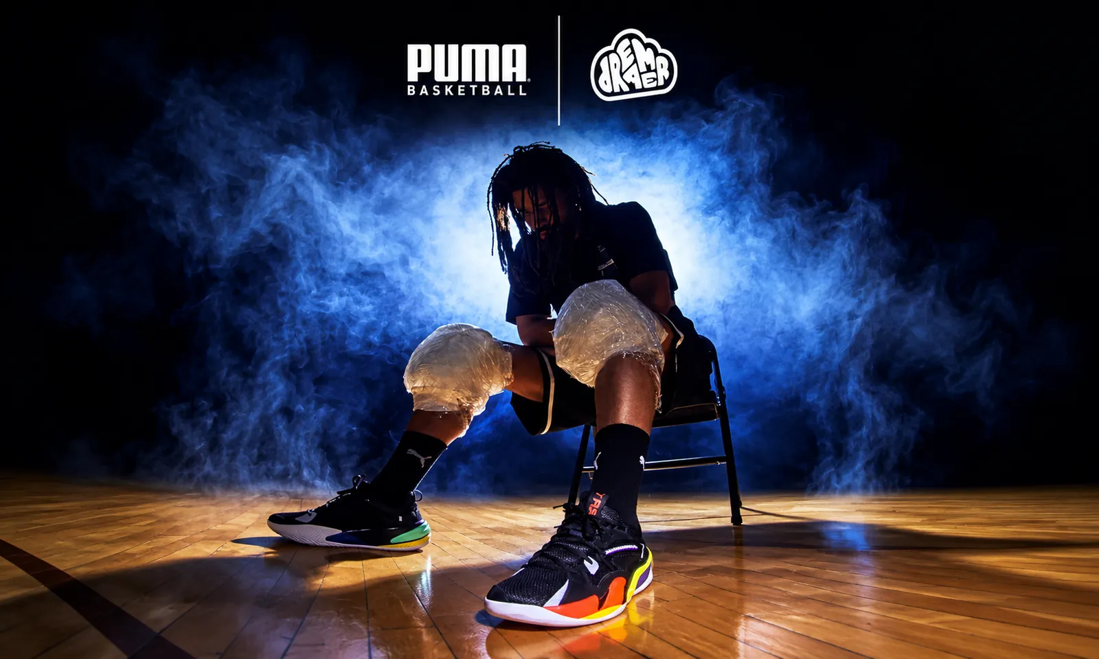 J. Cole seated on a basketball court wearing PUMA Dreamer sneakers